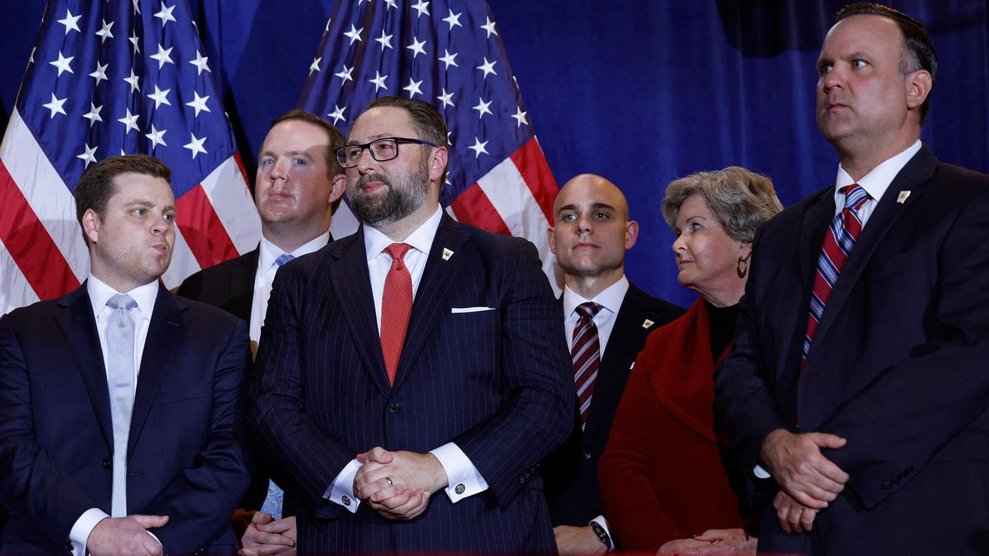 Fünf Männer in Anzügen und eine Frau im roten Blazer stehen auf einer Bühne: das Berater-Team von Donald Trump